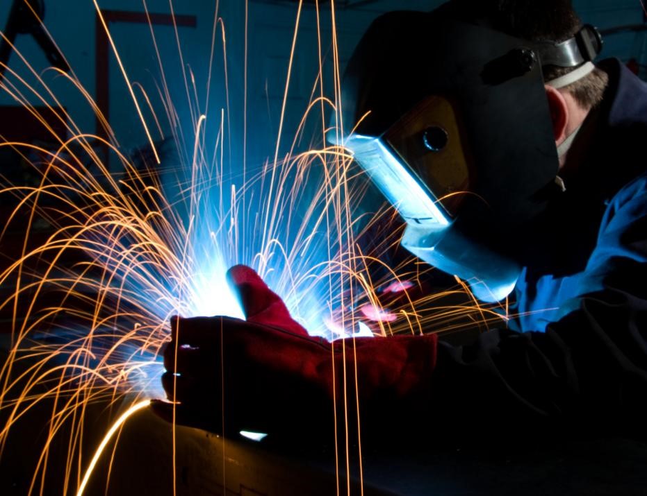 A professional welder performing metal fabrication work on a steel sheet.